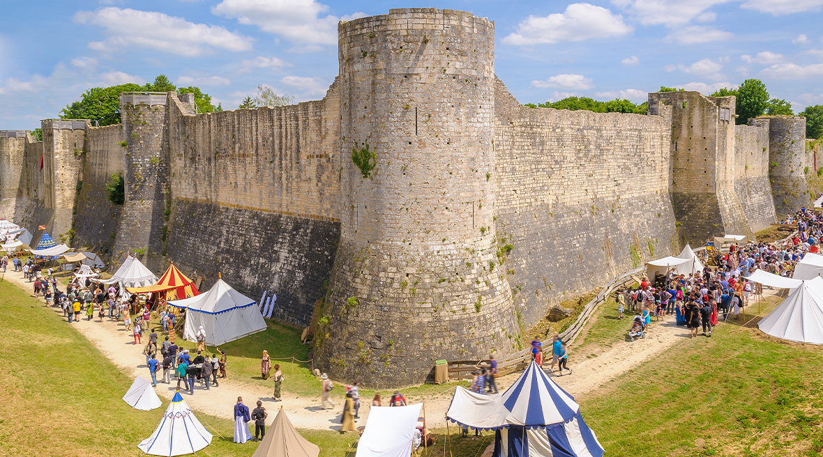 a festival with many tents and exhibits set up around a large stone wall with ramparts and towers